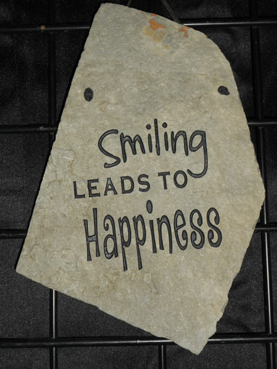 engraved rock sign that says smiling leads to happiness